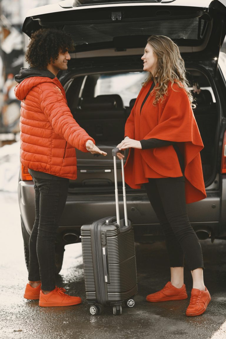 A couple stands by their car, packing luggage for a road trip.
